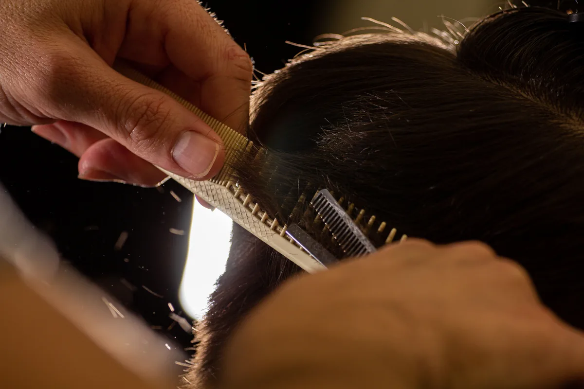 Les mains du coiffeur au peigne, sur une mèche en cours de travail
