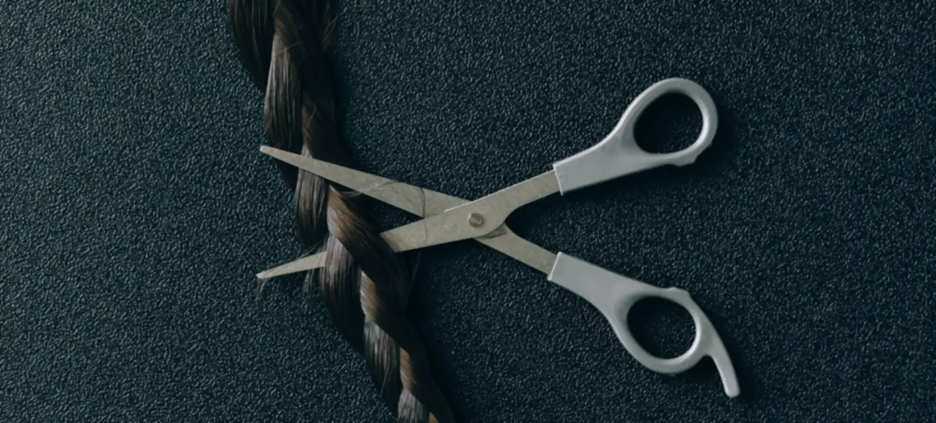 Ciseaux de coiffure posés à côté d'une tresse, sur un plan noir